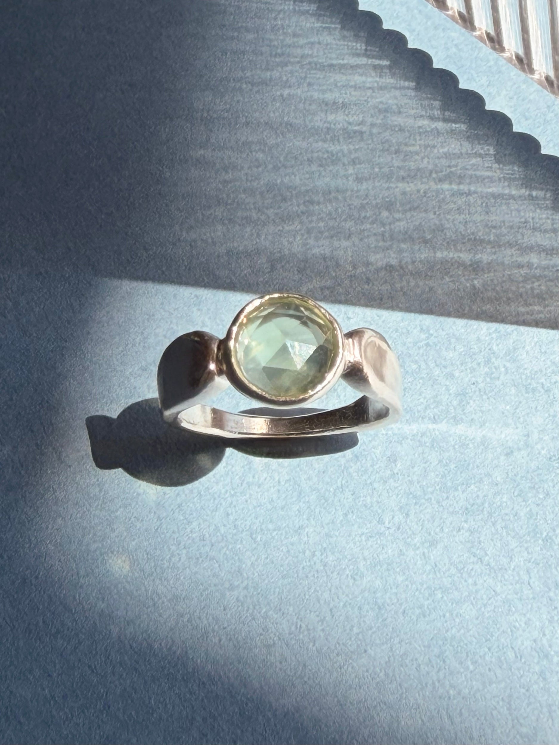 Pale green prehnite in a sculptural sterling silver ring on blue paper