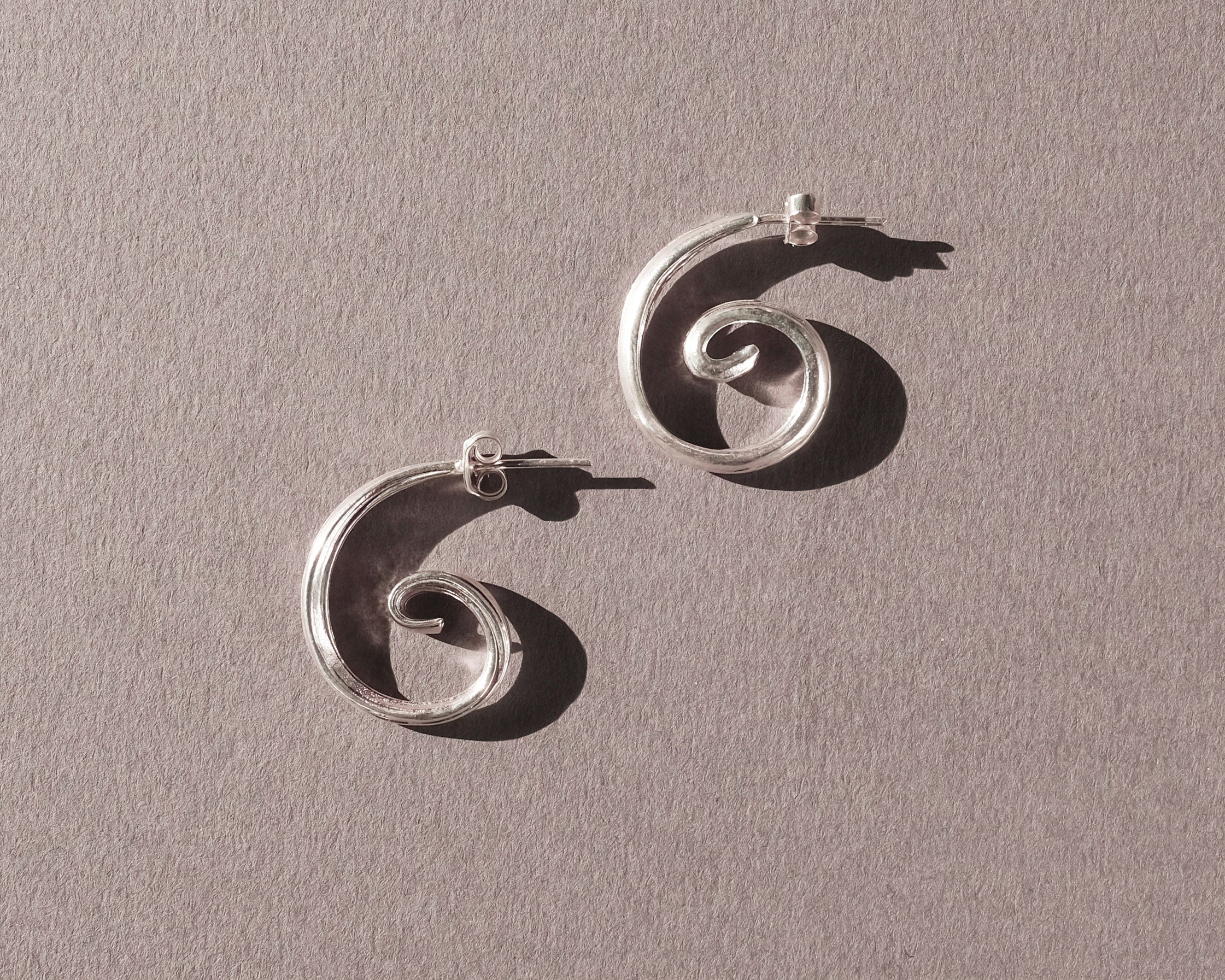 Pair of small sterling silver spiral earrings on grey paper