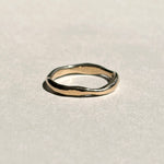 Thin sculptural 14k yellow gold wedding band on pale grey paper