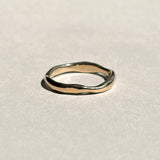 Thin sculptural 14k yellow gold wedding band on pale grey paper