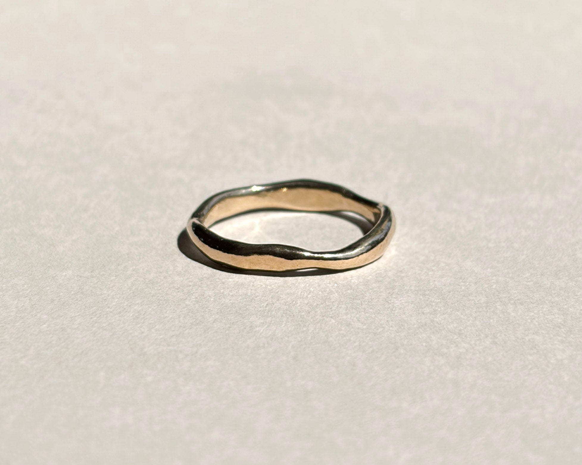 Thin sculptural 14k yellow gold wedding band on pale grey paper