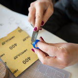 Hands shaping a blue wax ring with a carving tool during a RA HA jewelry workshop