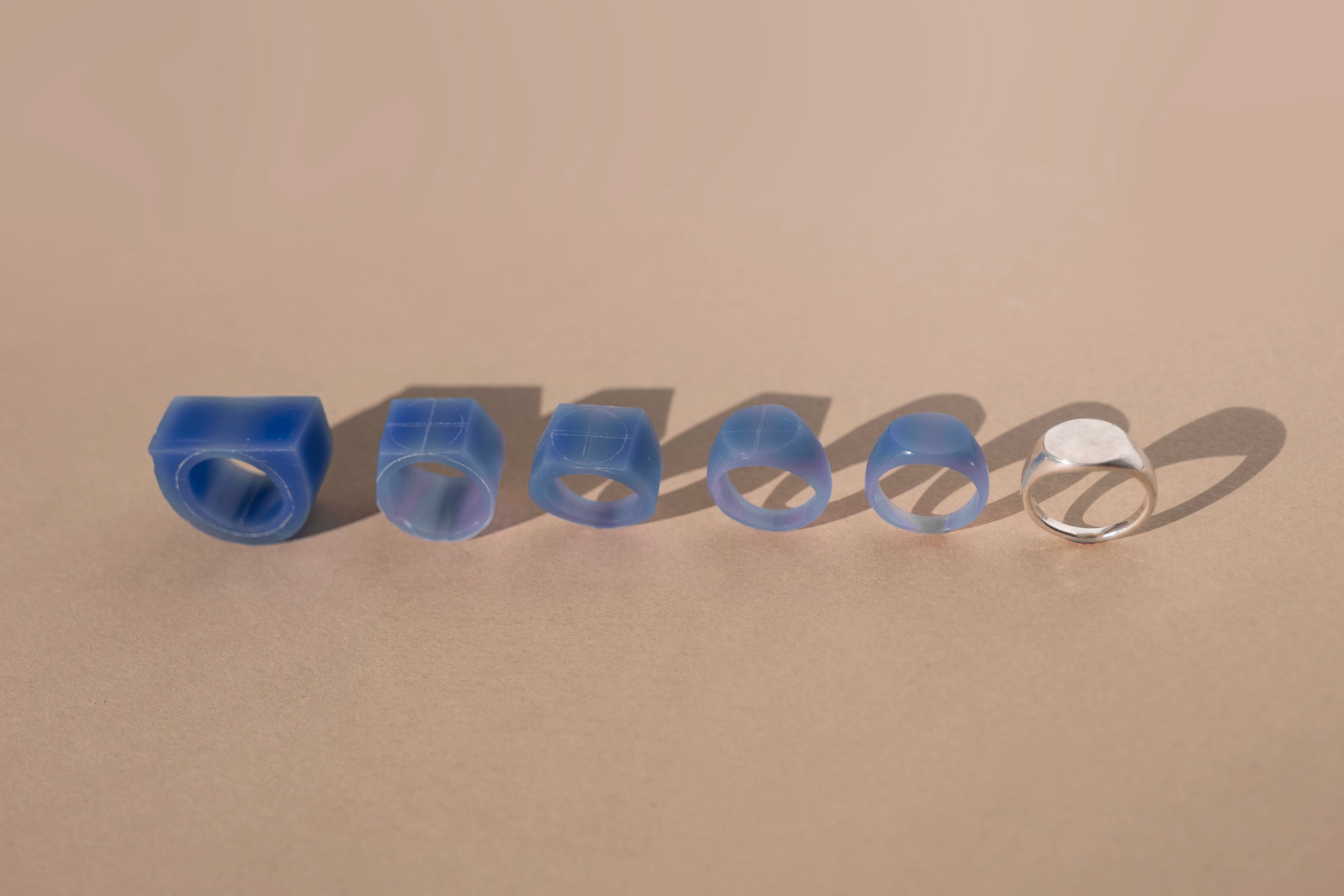 A sequence of hand-carved wax ring models progressing into a finished metal ring, showing the stages of the ring-making process.  Jewelry making class in Providence, RI