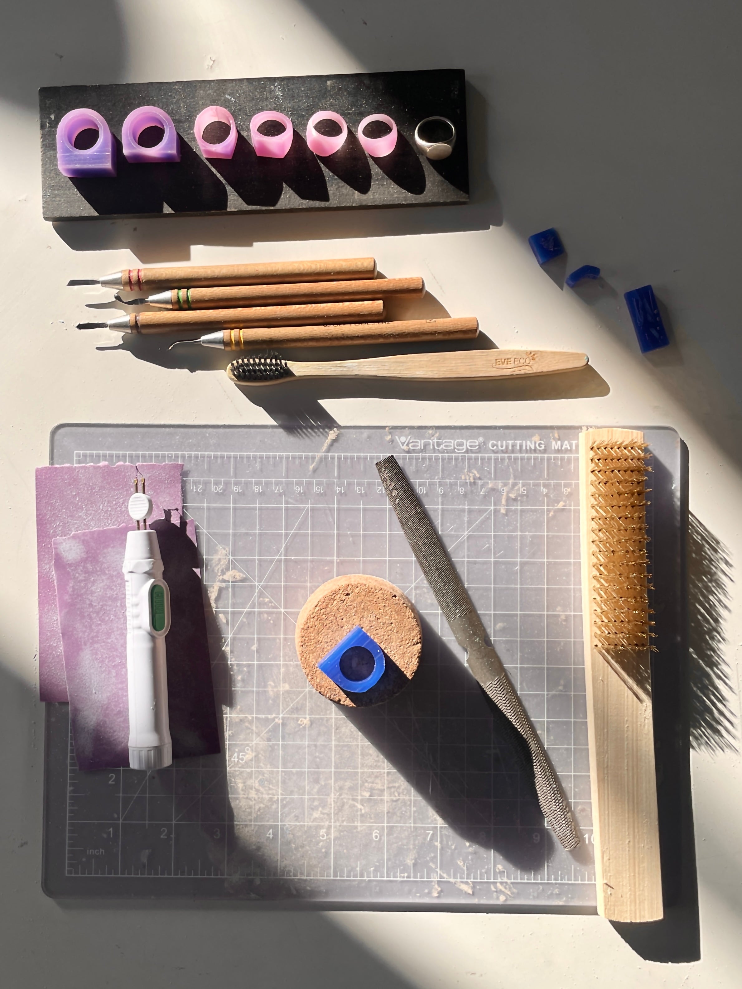 A set of wax carving tools, files, and ring models arranged on a work surface in a jewelry studio.
