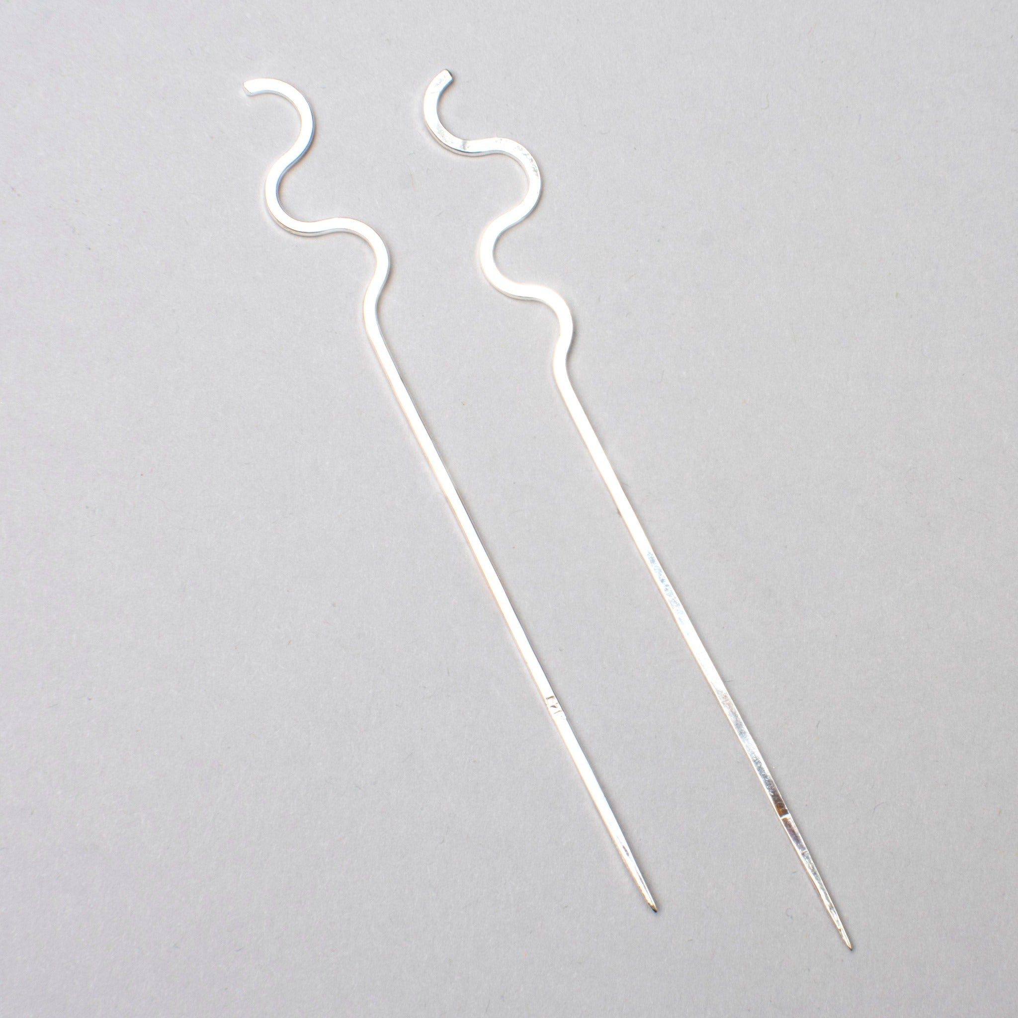 Two curvy sterling silver cocktail picks parallel on grey background